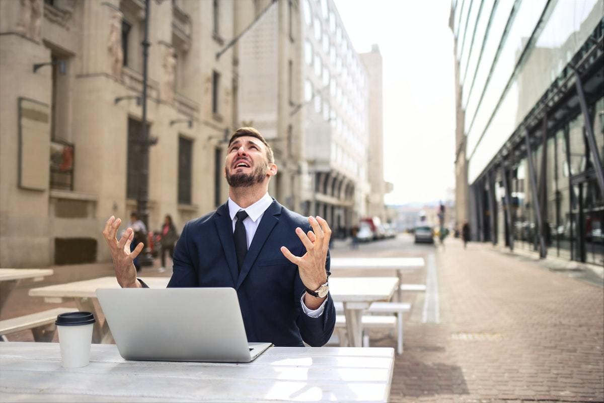 A man in a suit looking upward from his laptop in frustration