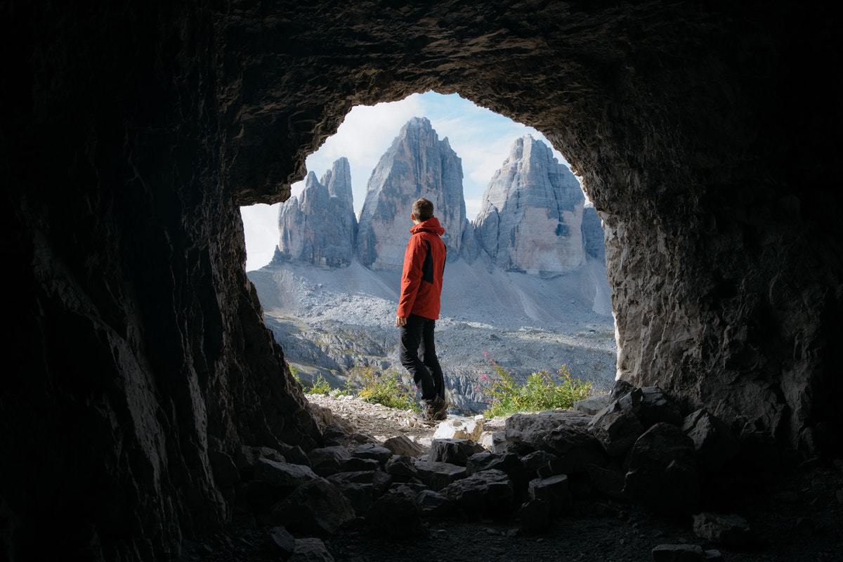 A man leaving a cave mouth into a landscape with mountains