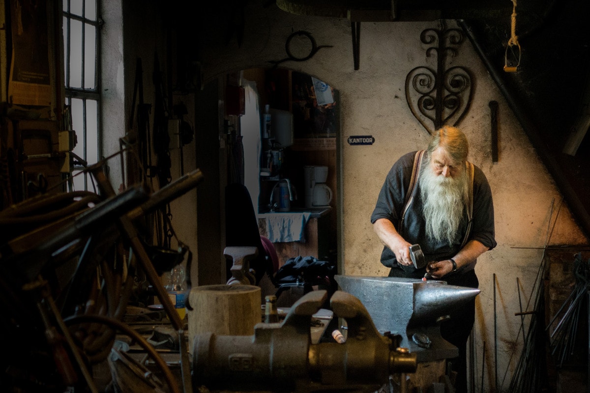 An old man with a long white beard working on an anvil